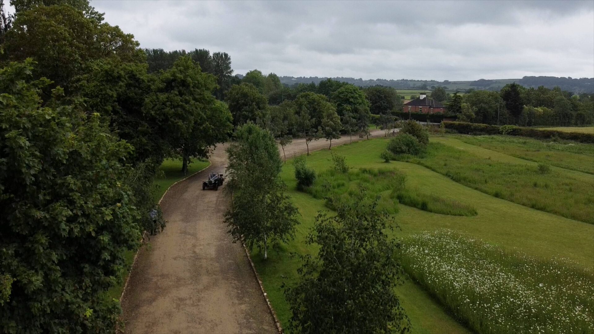 A newly married couple smiling inside a vintage 1920s Frazer Nash car arrive at Wharfedale Grange captured from a drone videographer