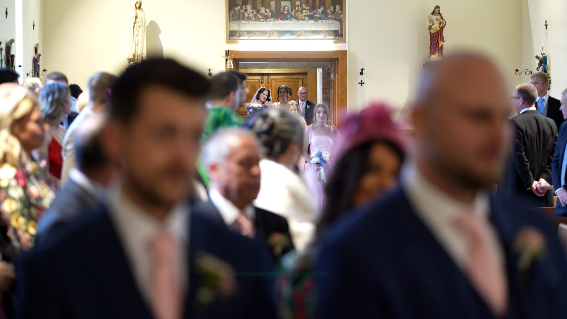 a documentary wedding videographer captures a first glimpse of the bride through the crowd during her wedding ceremony at St. Aelred's Catholic Church Harrogate