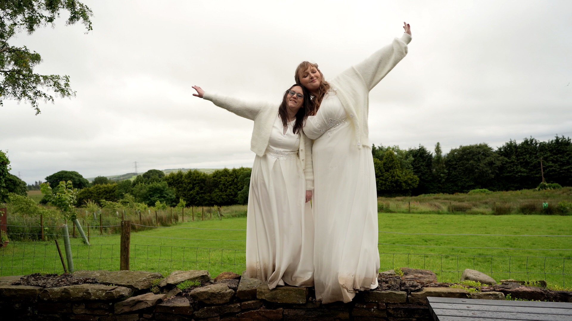 two brides stand and pose on a wall outside the wellbeing farm in Bolton Lancashire in the rain