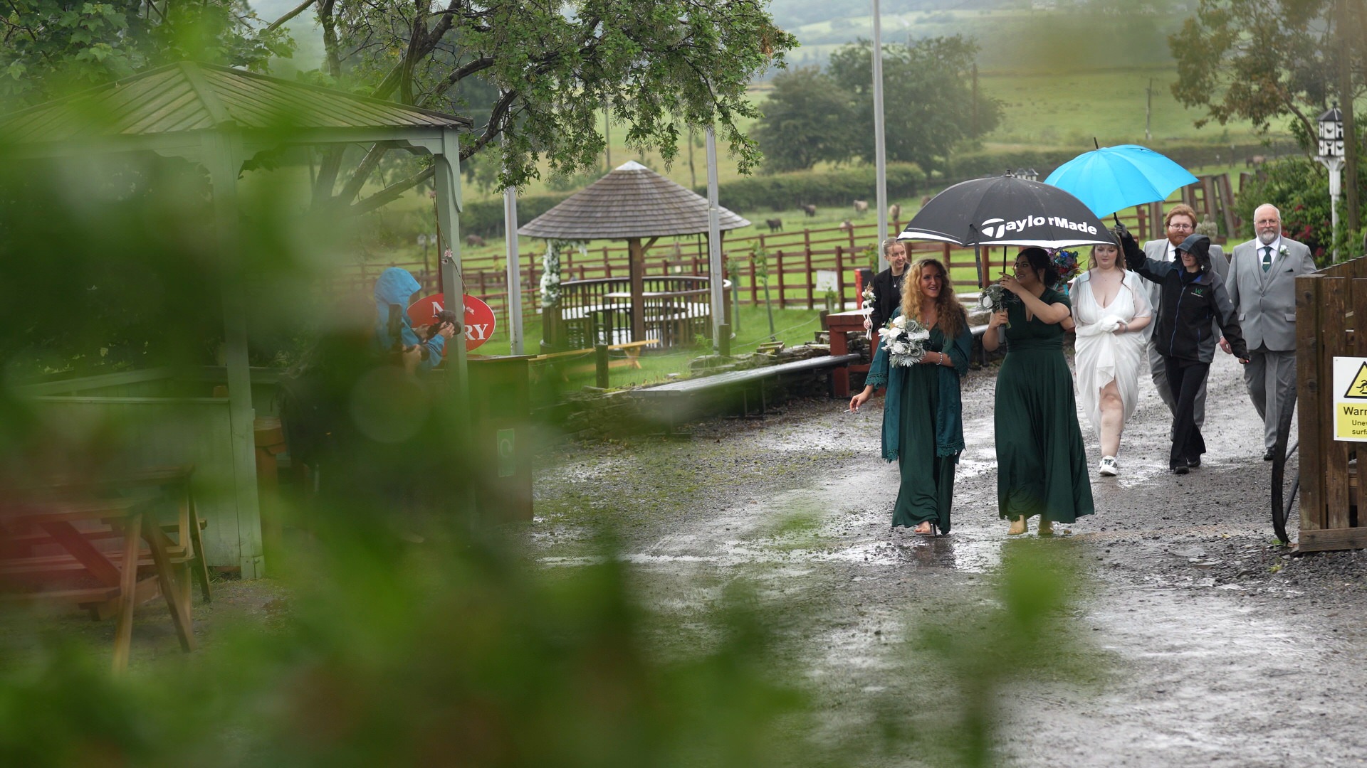 guests walk with umbrellas to the wedding barn at the wellbeing farm in Bolton Lancashire