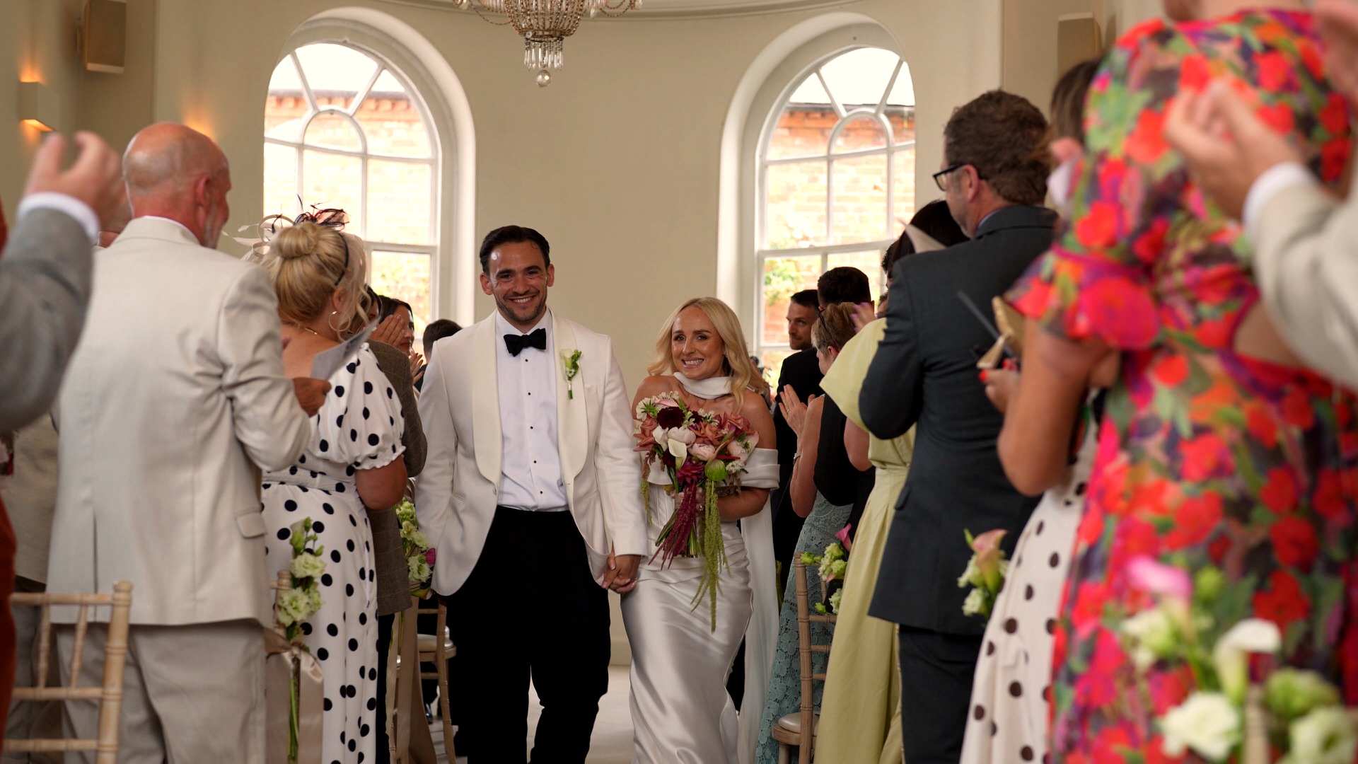the couple wearing a white dinner suit black tie and modern dress walk down the aisle