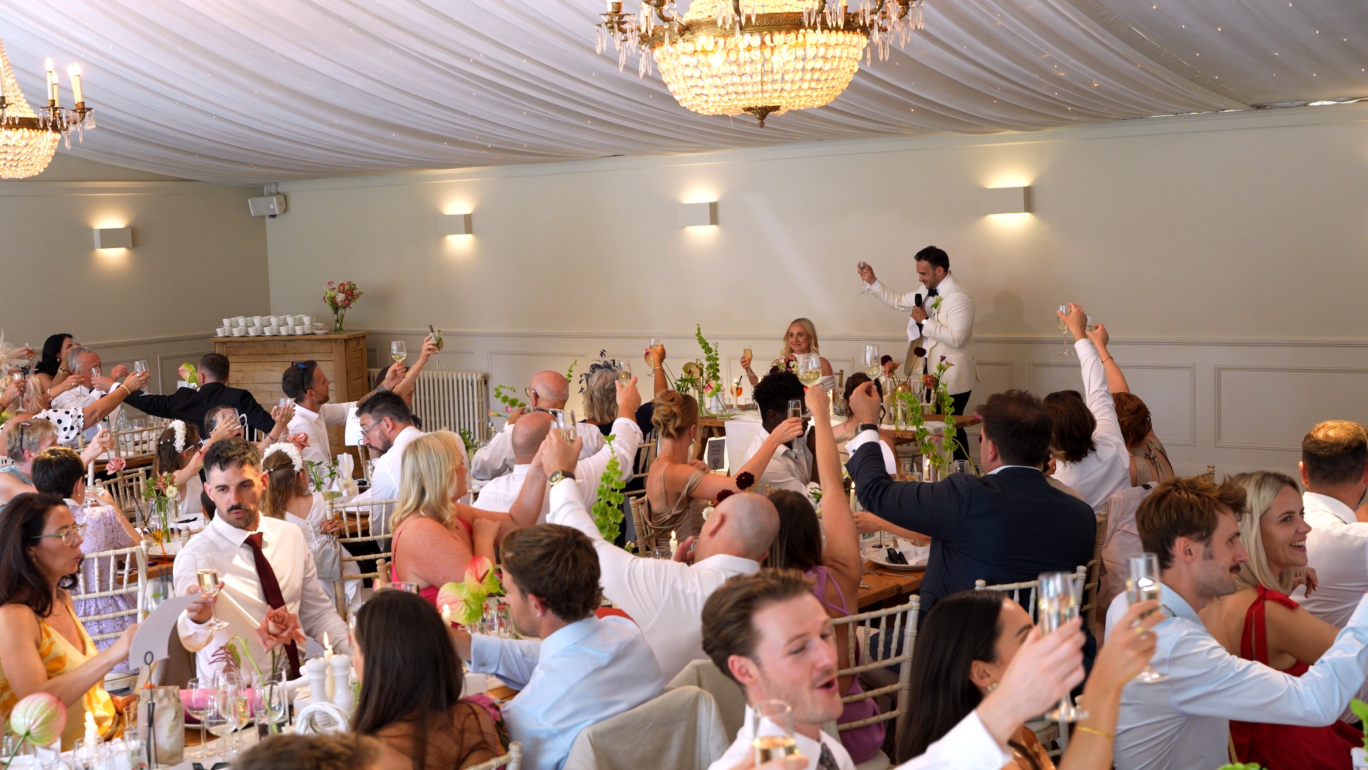 a wide shot of the guests sat on long banquet tables cheering the couple at Iscoyd Park