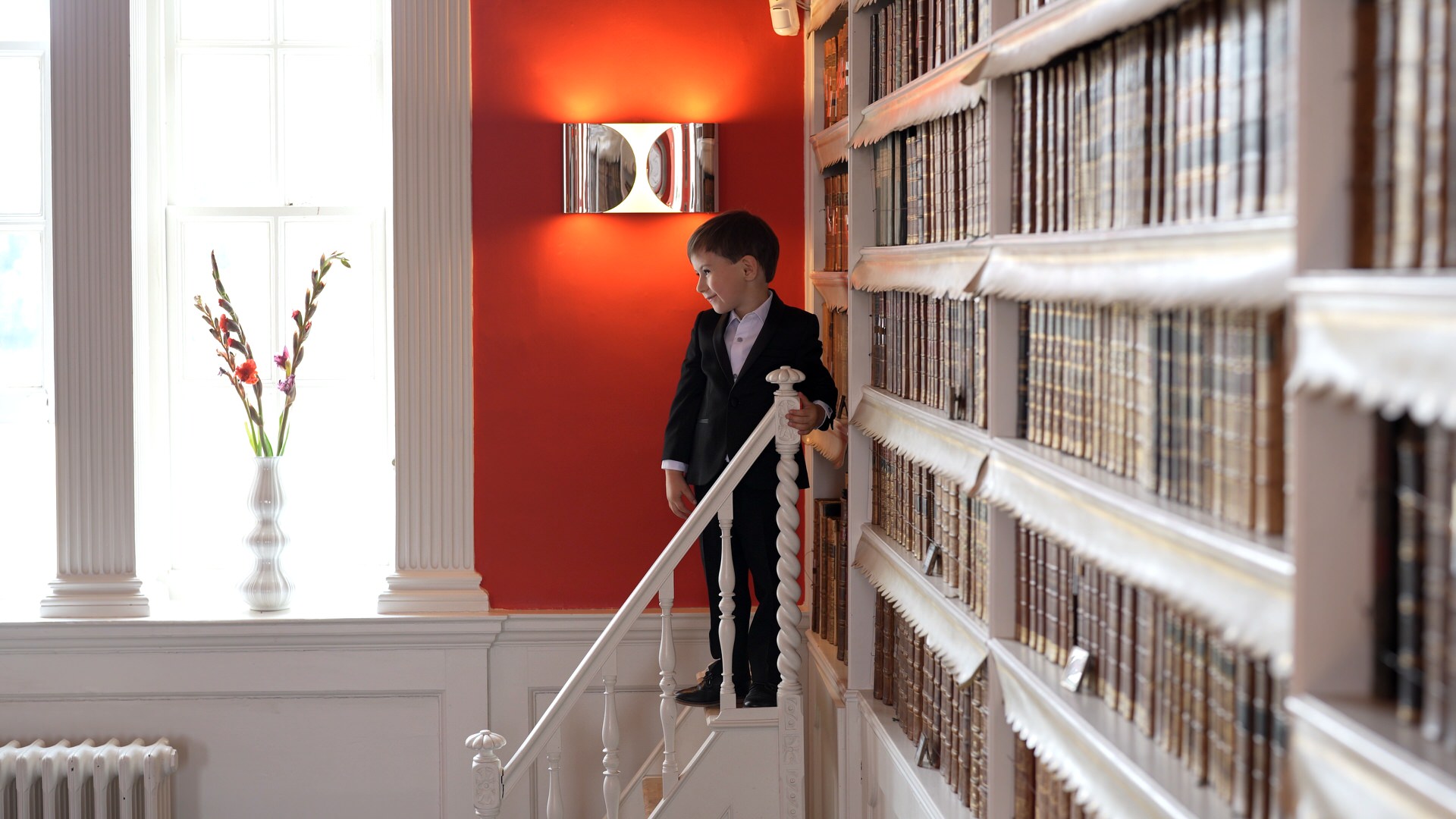 a page boy stands on the library steps inside groom prep at at Iscoyd Park